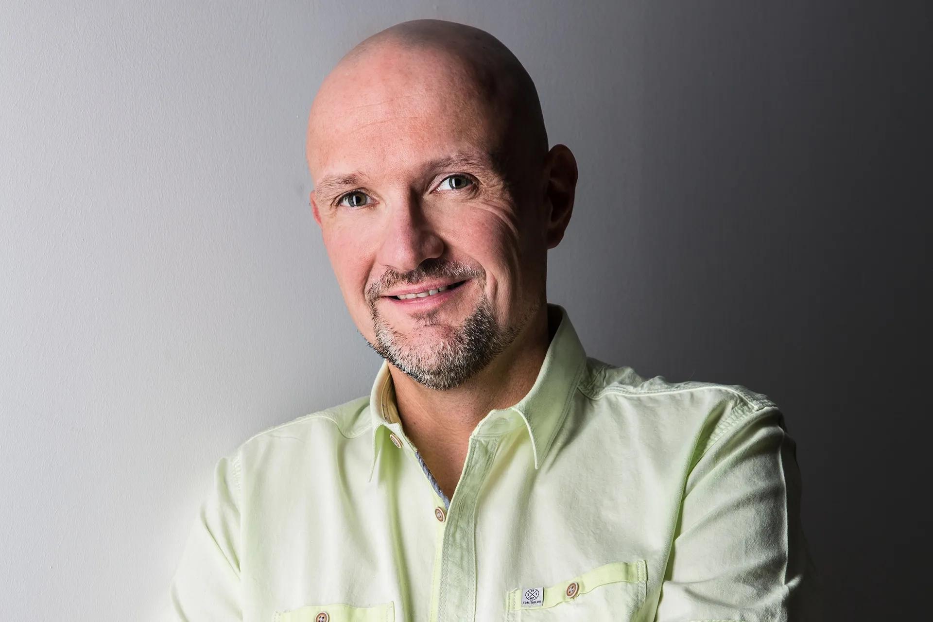 Bald man with a short beard smiles, wearing a light green collared shirt.